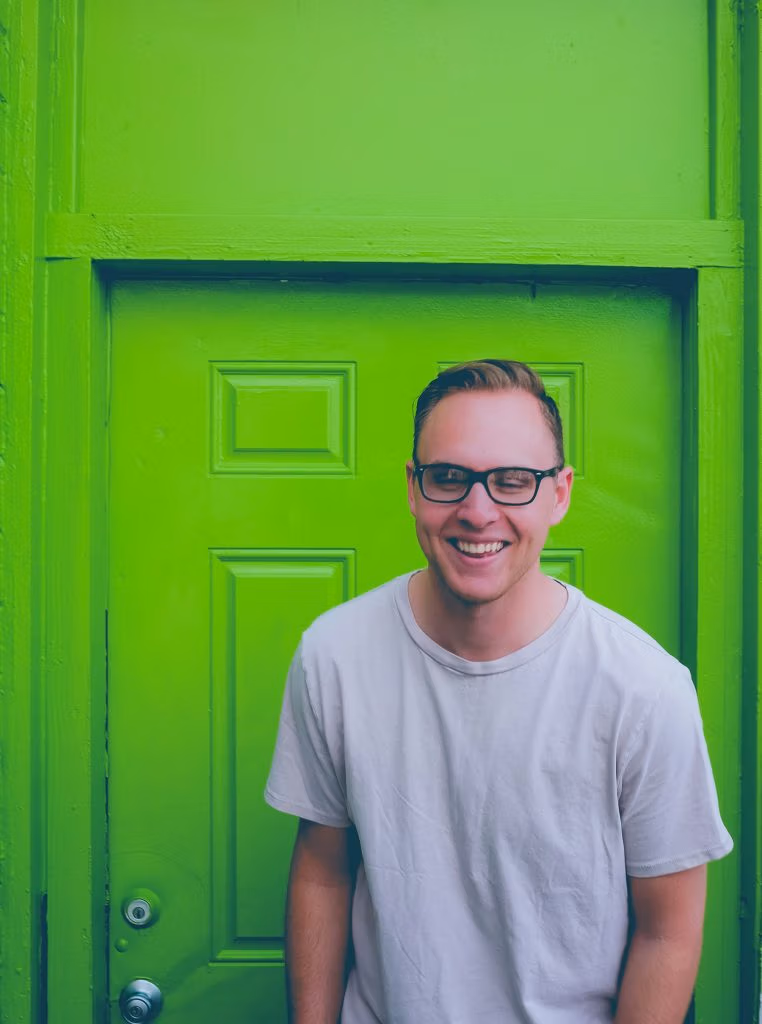 Homme souriant à lunettes devant une porte verte